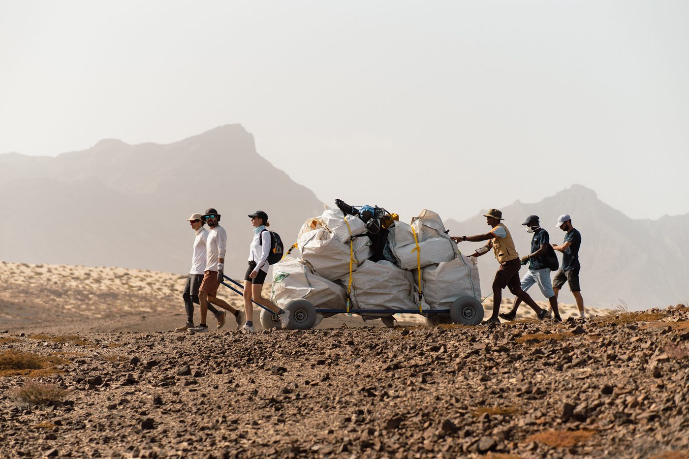 The crew hauls big bags of collected plastic across arid terrain on a beach cart.